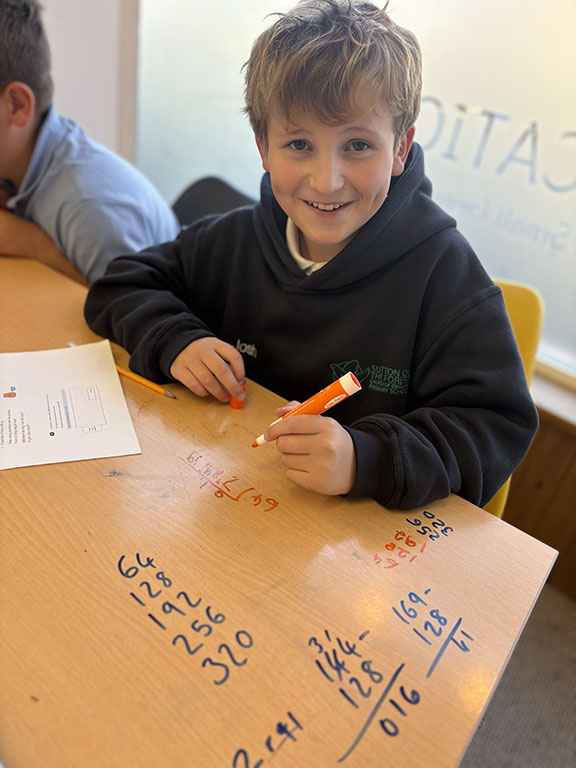 Pupil smiling while working through a maths practice activity in the EH Education classroom.